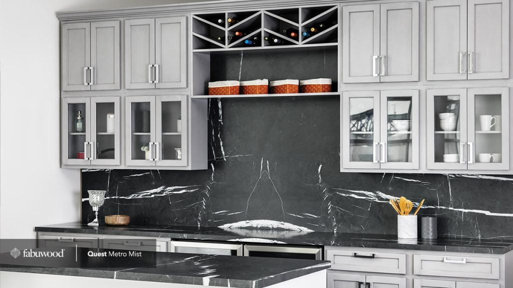 Mist traditional shaker kitchen cabinets with a black marble backsplash and black counters, glass front upper cabinets and a wine rack. Fabuwood Metro.